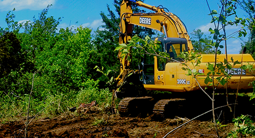Yellow excavator at well site surrounded by trees