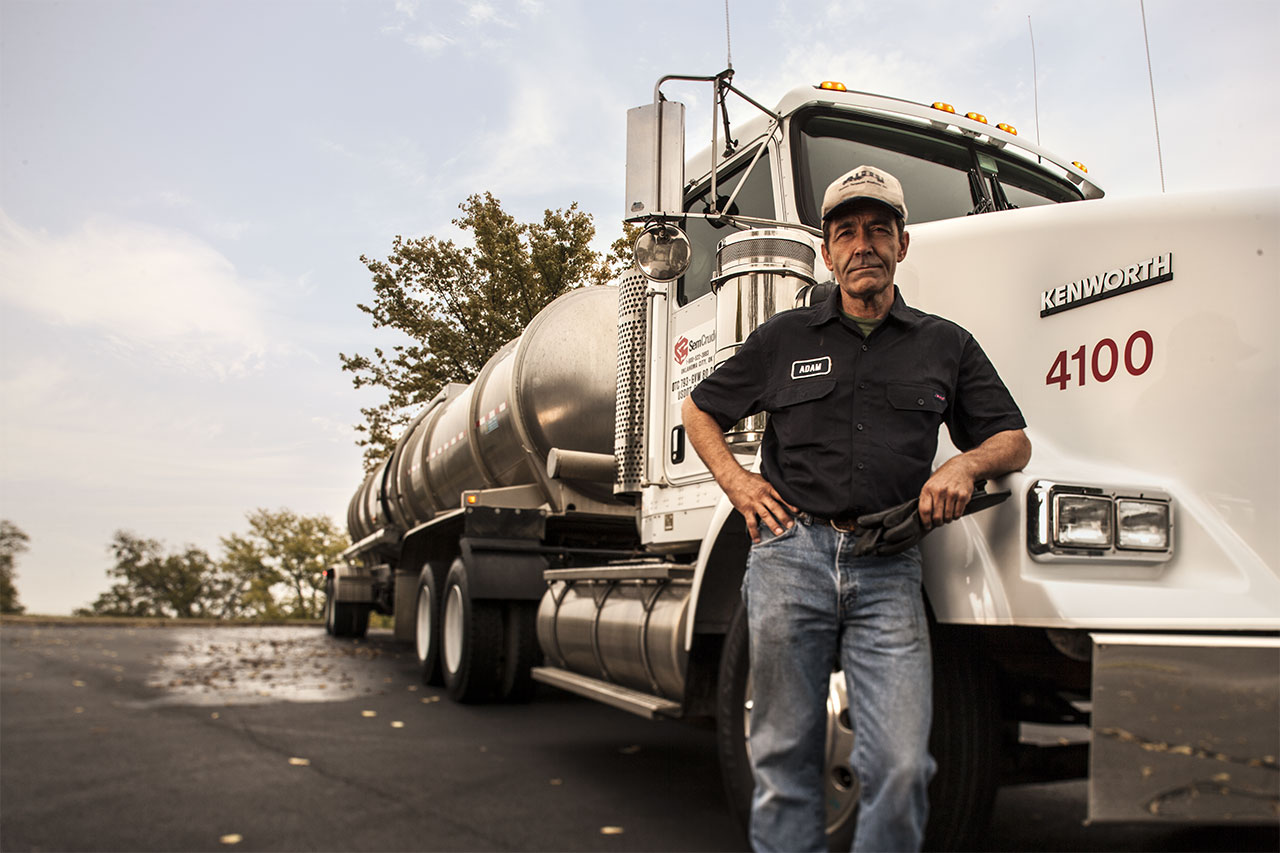 Man posing in front of an eighteen wheeler truck.