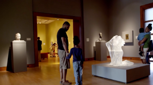 young son holding father's hand while looking at a white sculpture in a museum room