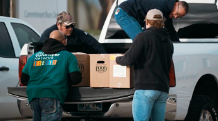 three men loading cardboard boxes into the bed of a white truck