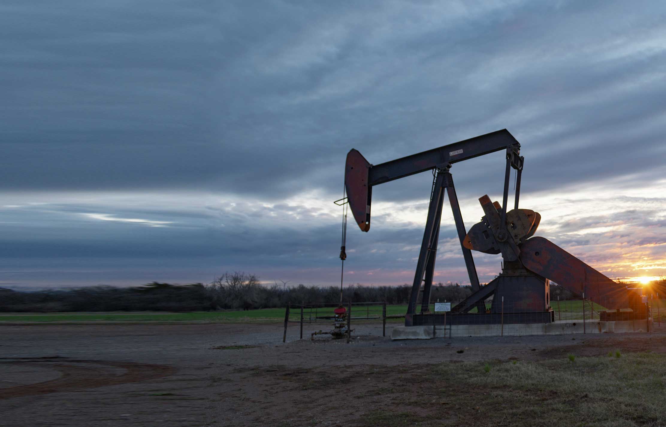 Sun is setting with cloudy gray skies with a pump jack