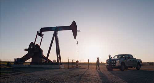 Sun setting in the distance while a worker walks toward a pump jack
