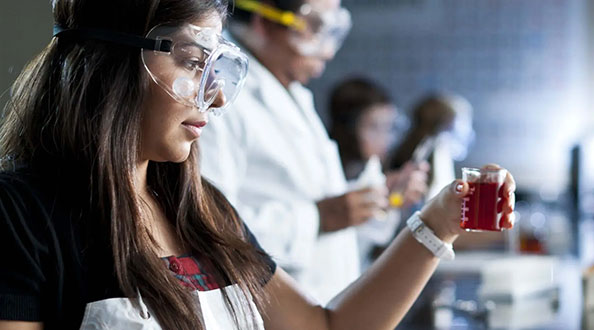 Student in safety glasses holding a beaker with red liquid