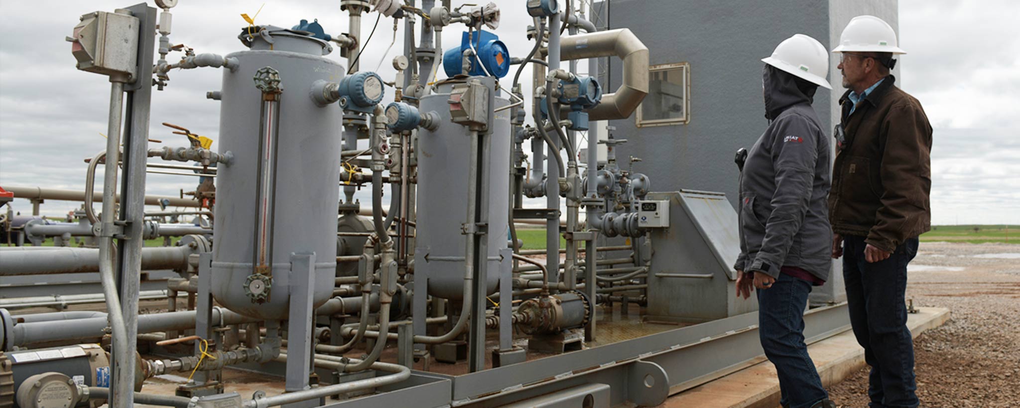 Two technicians in the field standing beside oil machinery