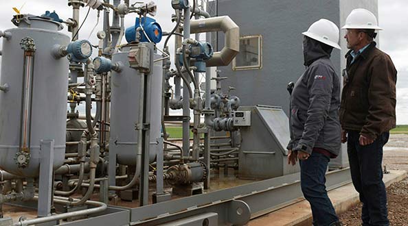 Two technicians in the field standing beside oil machinery