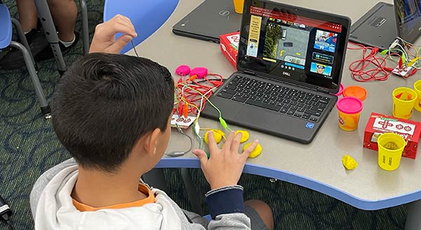 A student works with wire, clay and a small laptop in an experiment