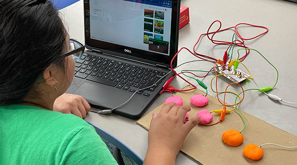 Girl experimenting with a computer and wiring at a STEM Maker Camp