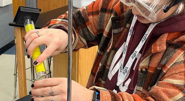 Student wearing goggles pouring liquid from a test tube